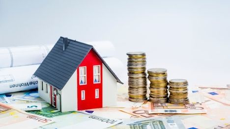 Ein Modellhaus mit Geldscheinen und Geldmünzen