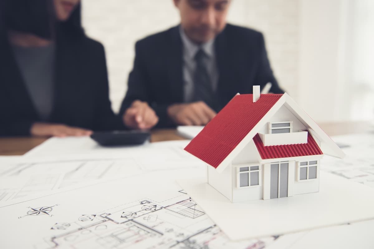 Geschäftsleute sitzen vor mehreren Zetteln und einem Modellhaus